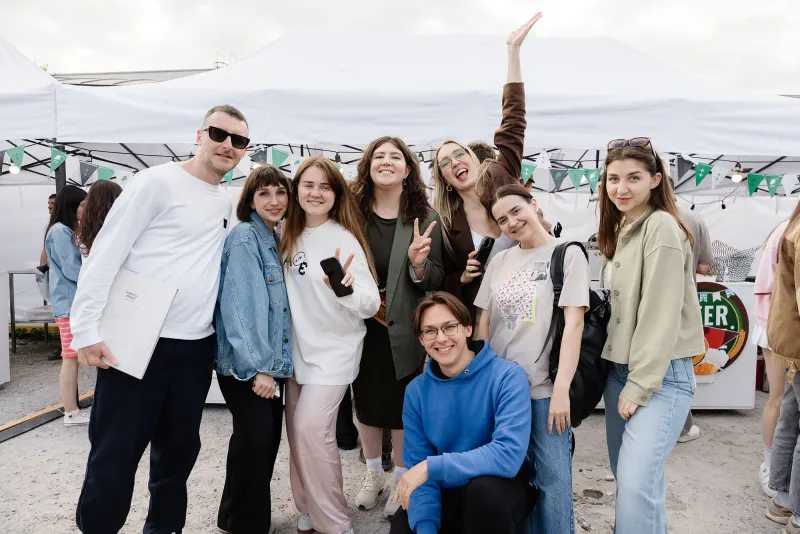 Group of friends posing in front of white festival tents, one with an arm raised
