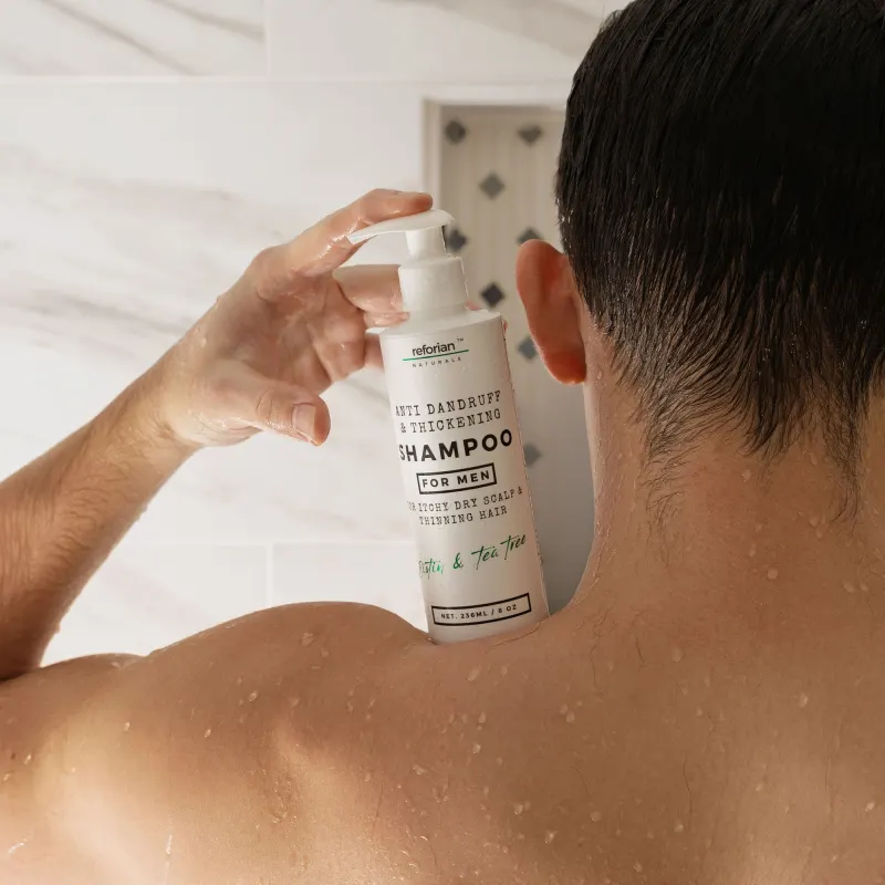 Man in the shower seen from behind, holding a bottle of anti-dandruff shampoo