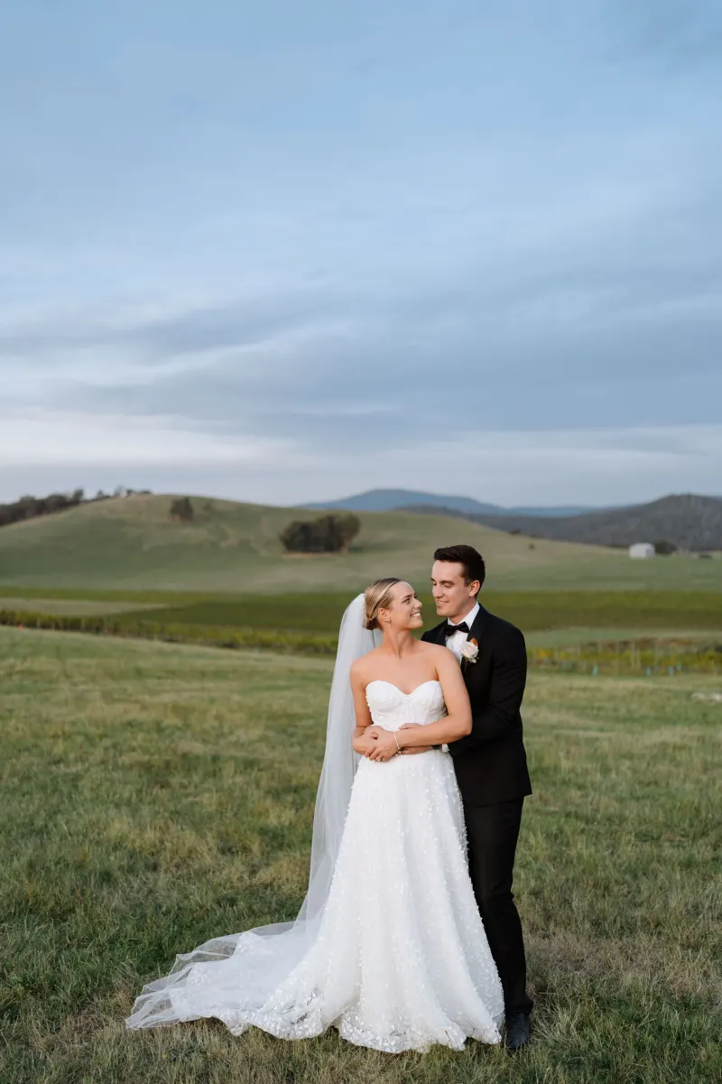 Couple standing together in an open field of rolling green hills under a wide clouded sky